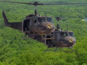 Two military helicopters flying over a forest.
